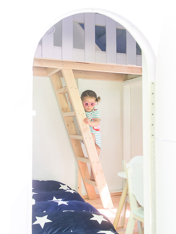 Young girl descending a wooden ladder inside a playhouse