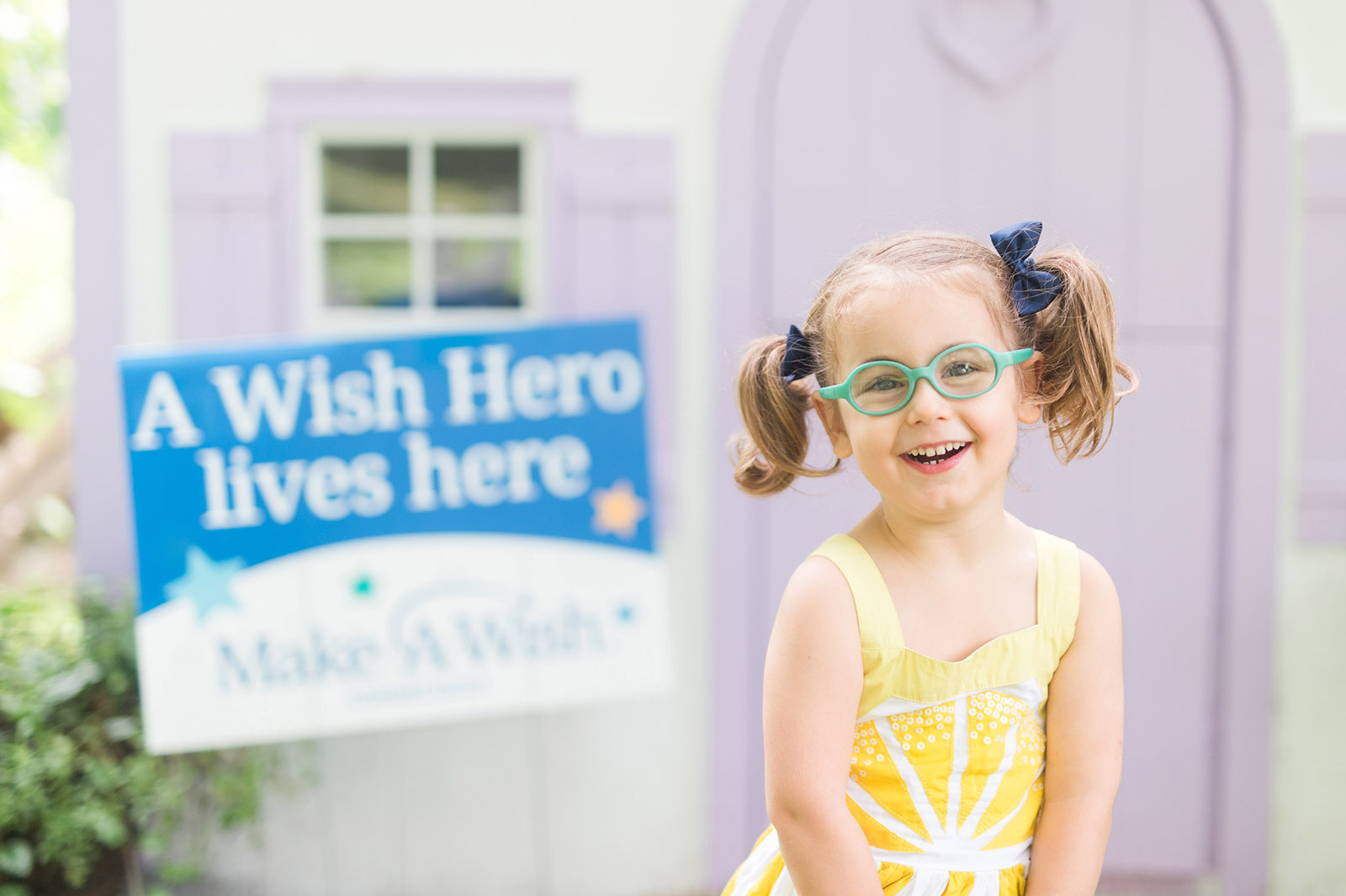 Young girl standing in front of a playhouse with a purple door.