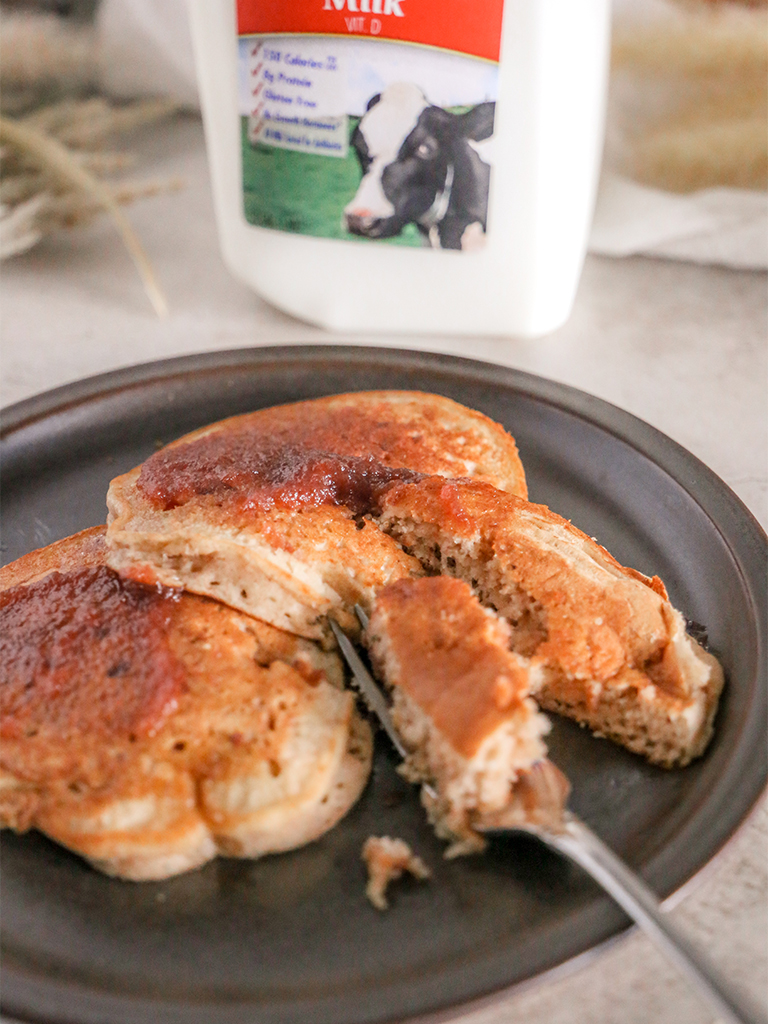 A plate of apple butter pancakes with a bite cut out, served in front of a bottle of Hiland Vitamin D Milk, featuring a cow on the label.