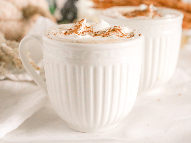 Creamy pumpkin white hot chocolate topped with whipped cream and cinnamon, served in a cozy white mug for a festive treat.