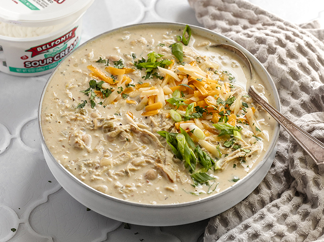 Rich white chicken chili topped with shredded cheese and green onions, served in a bowl for a hearty and comforting meal.