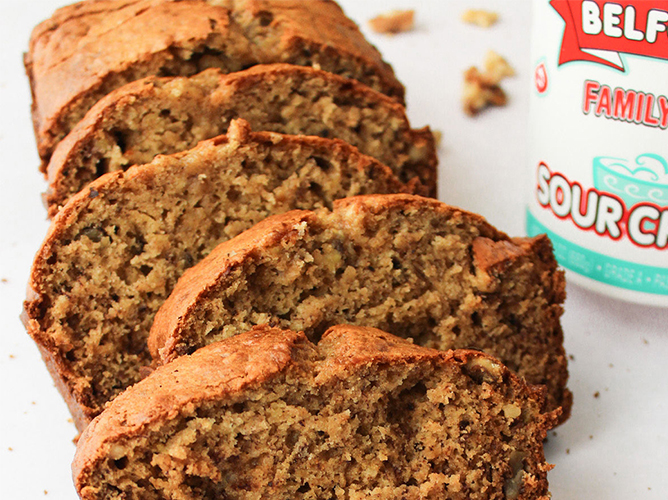 Slices of moist banana bread are displayed next to a carton of Belfonte sour cream, highlighting a classic homemade treat.