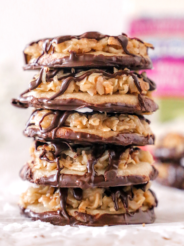 A stack of caramel coconut shortbread cookies drizzled with dark chocolate, with a crisp, golden shortbread base topped with toasted coconut caramel drizzle.